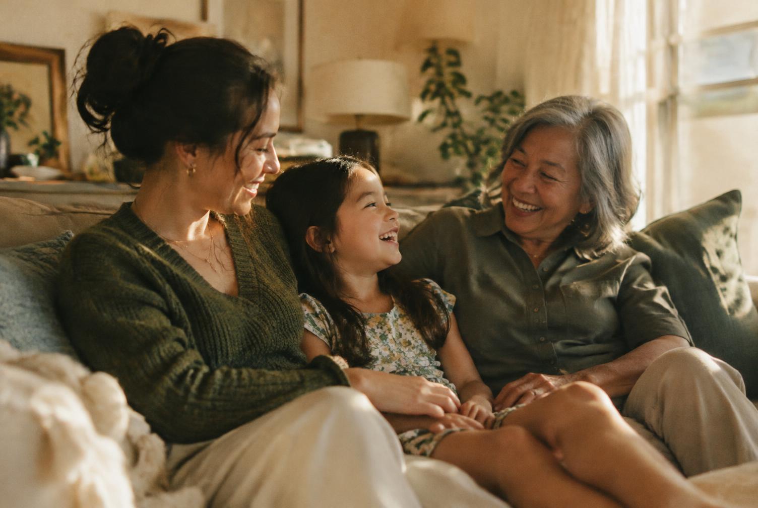 A mother, daughter and grandmother laughing together on a couch